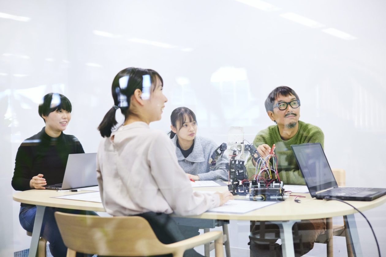 A group of people with laptops sitting around a table with robotic hardware between them
