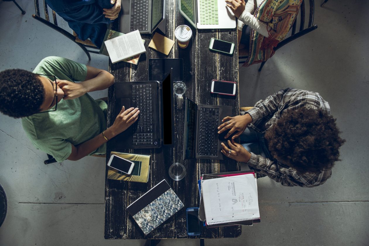 Aerial view of people working on laptops at a table with notebooks next to them