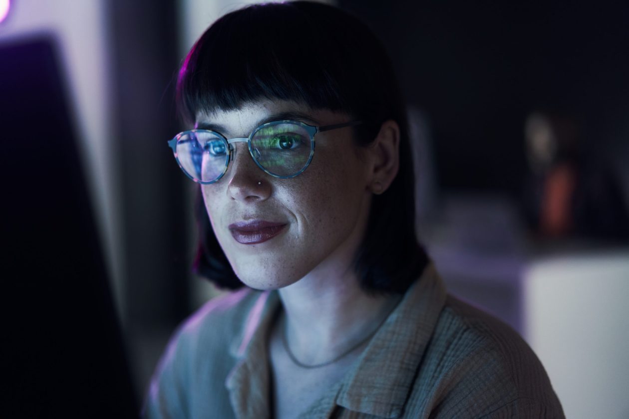 Business woman, computer ai and coding of young employee with blue light and glasses. Digital code, hacker face and reading of a female employee at night planning with online cybersecurity data