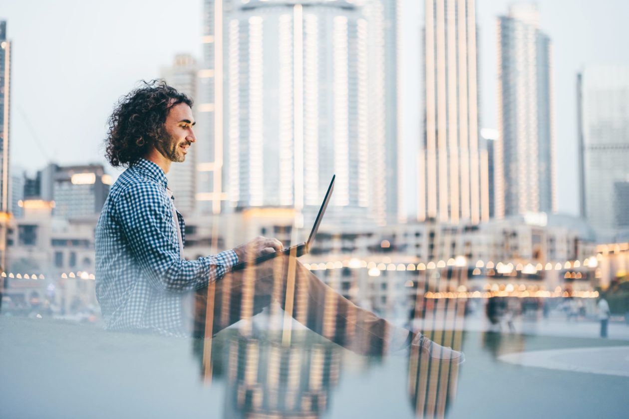 Man uses laptop against the backdrop of a cityscape in the city park.