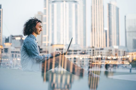 Man uses laptop against the backdrop of a cityscape in the city park.