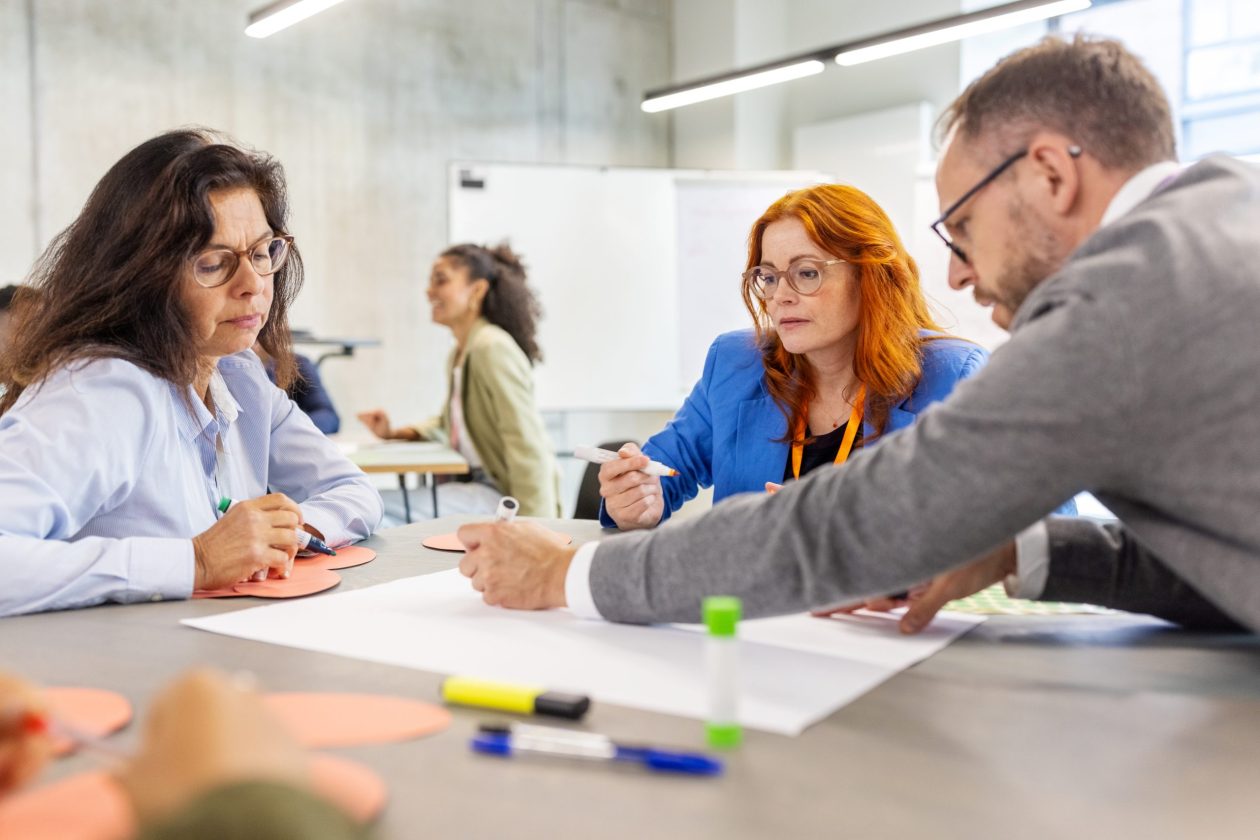 Diverse group of professionals seated together at a table, participating in interactive seminar activities. Reflects inclusivity, collaboration, and focused teamwork at a convention center event.