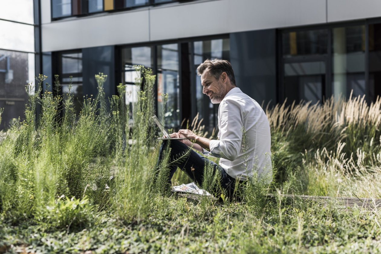 Man smiling with his laptop outside amongst the tall grass