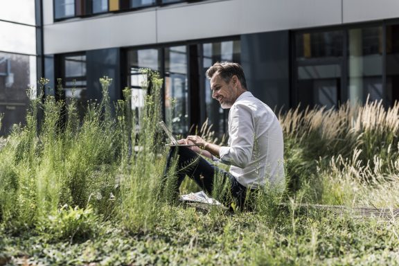 Man smiling with his laptop outside amongst the tall grass